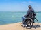 Disabled young man sitting in a wheelchair and looks at the sea