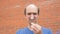 Disappointed balding man pulls seeds from a dandelion. brick wall background