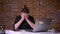 Disappointed caucasian male in black suit covers face with his hands looking at laptop and sitting near brick wall