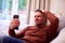 Disappointed Mature Man At Home Relaxing On Sofa Watching Sport On Mobile Phone