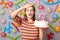 Disappointed woman in striped dress with dirty face standing against gray wall decorated with colorful balloons forgot making
