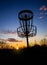 Disc golf basket against sunset