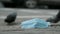 Discarded medical face mask lies on the sidewalk, on the background pigeons walk and cars drive. Face masks polluting streets of t