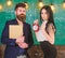 Discipline concept. Man with beard hold book and girl teacher holds alarm clock, chalkboard on background. Lady