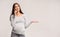 Discontented Pregnant Girl Talking On Phone Standing Over Gray Background