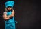 Disgruntled little girl dressed in blue cook uniform standing with crossed arms. on dark textured background.