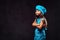 Disgruntled little girl dressed in blue cook uniform standing with crossed arms. Isolated on dark textured background.