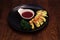 Dish of grilled cheese served with raspberry sauce on black plate, wooden background. Delicious cheesy dish served in