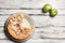 A dish with a notched pie and two green apples on a wooden surface