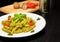 Dish of pasta with pesto genovese sauce and vegetables, tomato and basil on black wood table