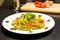 Dish of pasta with pesto genovese sauce and vegetables, tomato and basil on black wood table