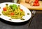 Dish of pasta with pesto genovese sauce and vegetables, tomato and basil on black wood table near fork