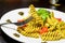 Dish of pasta with pesto genovese sauce and vegetables, tomato and basil, detail of fork with fusilli on top