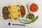 Dish with spaghetti, cutlet, beans, onion and olives, bowls with beans, green olives, fork on table. Top view