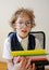 Disheveled little schoolboy holding a stack of textbooks and smiles.