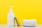 Dishwashing detergent in white bottle, pile of saucers and cleaning sponge against yellow background