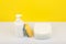 Dishwashing detergent in white bottle, pile of saucers and cleaning sponge against yellow background