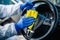 Disinfection professional cleans up a steering wheel of a car with a yellow rug. Sanitary service worker disinfects the vehicle`s