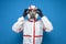 Disinfector man in a protective suit puts on a mask and glasses on a blue isolated background, disinfection service worker,