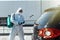 Disinfector in a protective suit conducts disinfection in contaminated area of car to prevent coronavirus. Health care