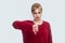 Dislike. Portrait of dissatisfied sad beautiful young blond woman in red blouse standing with thumbs down and looking at camera