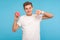 Dislike to junk food! Dissatisfied unhappy man in t-shirt showing thumb down and holding sweet doughnut