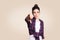 Dislike. Young unhappy upset girl with casual style and bun hair thumbs down her finger, on beige blank wall with copy space