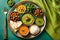 Display a colorful vegetarian thali against a green-toned backdrop with ample copy space