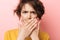 Displeased beautiful woman posing  over pink wall background covering mouth