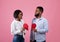 Displeased black guy and lady holding halves of torn paper heart on pink studio background. Divorce or breakup concept