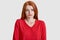 Displeased ginger lady frowns face, has freckled skin, wears red jumper, doenst like something, models over white background,