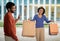 Displeased Husband Looking At Happy Wife With Shopper Bags Outdoors