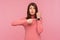 Displeased impatient woman with brown hair in pink sweater pointing finger on her wrist clock looking at camera with anxious,