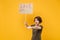 Displeased protesting woman hold protest sign broadsheet placard on stick pointing finger aside isolated on yellow