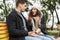 Displeased stressed young loving couple drinking tea or coffee outdoors in park talking with each other quarrel