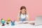 Displeased tired little kid schoolgirl 12-13 years old study at white desk with pc laptop isolated on pink background