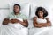 Displeased unhappy millennial african american woman suffers from noise and snoring of sleeping husband on bed