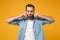 Displeased young bearded man in casual blue shirt posing isolated on yellow orange wall background studio portrait