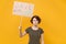 Displeased young protesting woman hold protest sign broadsheet placard on stick isolated on yellow background studio