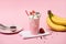 Disposable cup of milkshake with chocolate chips and strawberries on napkins near bananas and plate with scoop
