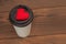 Disposable cups for beverages and red heart on wooden background.