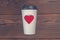 Disposable cups for beverages and red heart on wooden background. Toned photo.