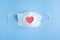 Disposable medical mask on blue background with red heart