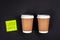 Disposable paper cups and paper sticker on a dark background, top view.