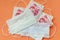 Disposable protective masks and cash chinese money on orange background. Concept of medicines deficiency, personal
