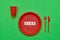 Disposable red plastic plate with word STOP inside, red knife and fork on green background. Top view, copy space. Plastic free