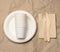 Disposable round white paper plates and cups on brown paper background, top view