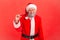 Dissatisfied elderly gray bearded man in santa claus costume showing a little gesture with fingers, skeptical about winter