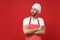 Dissatisfied male chef cook baker man in striped apron white t-shirt toque chefs hat posing isolated on red background