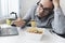 dissatisfied man eating instant noodles while working with laptop in office. Lunch at the office. tasteless junk food